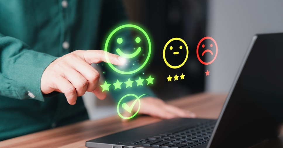 Mão seleciona ícone de sorriso em tela sobre perguntas para pesquisa de satisfação.